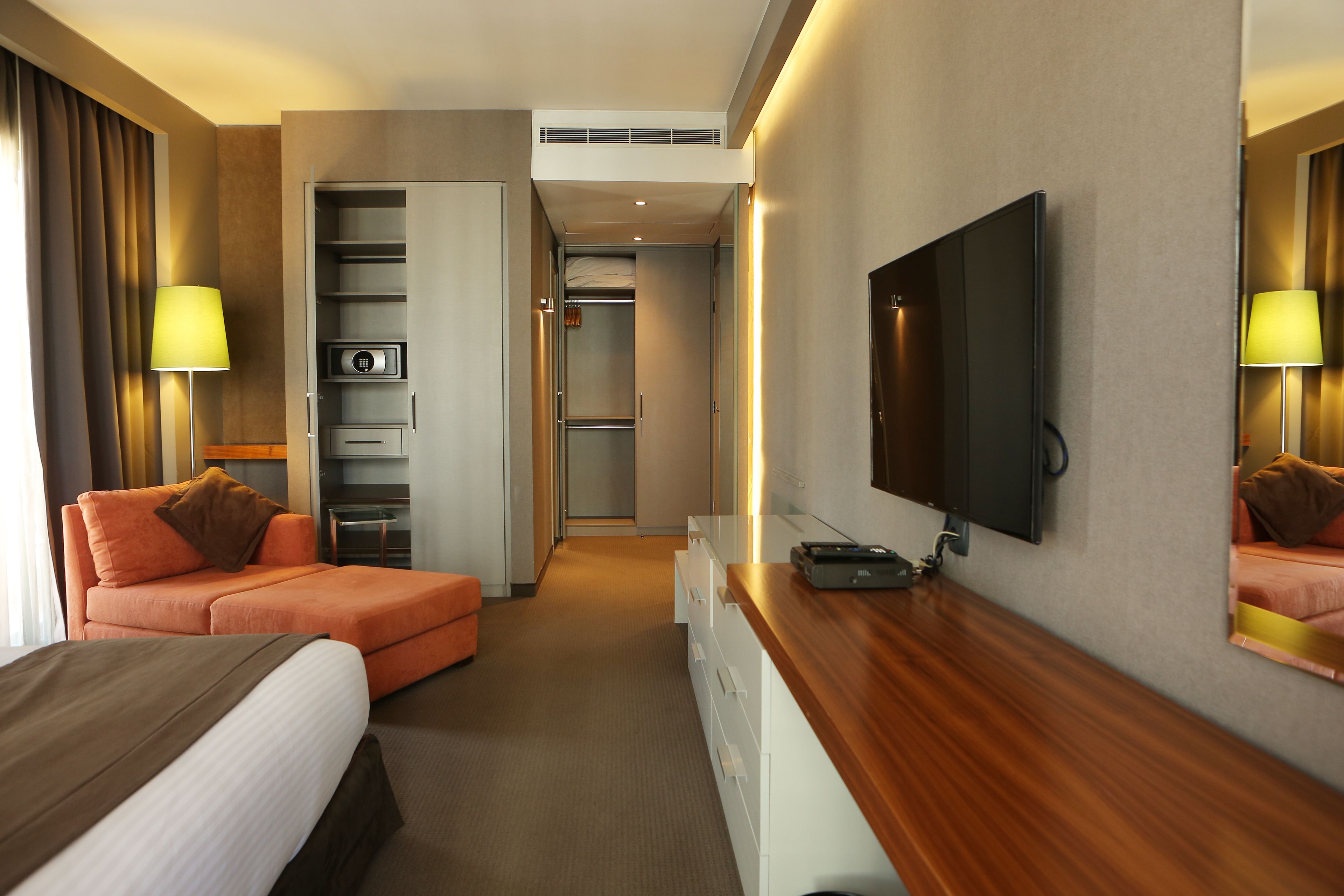 A hotel room with a bed, a sofa, a TV, a desk, and a wardrobe.