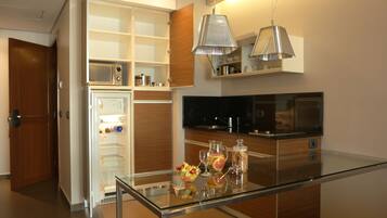 Una cocina moderna con refrigerador, microondas y horno integrados. Hay una mesa de vidrio con un frutero y una jarrón.