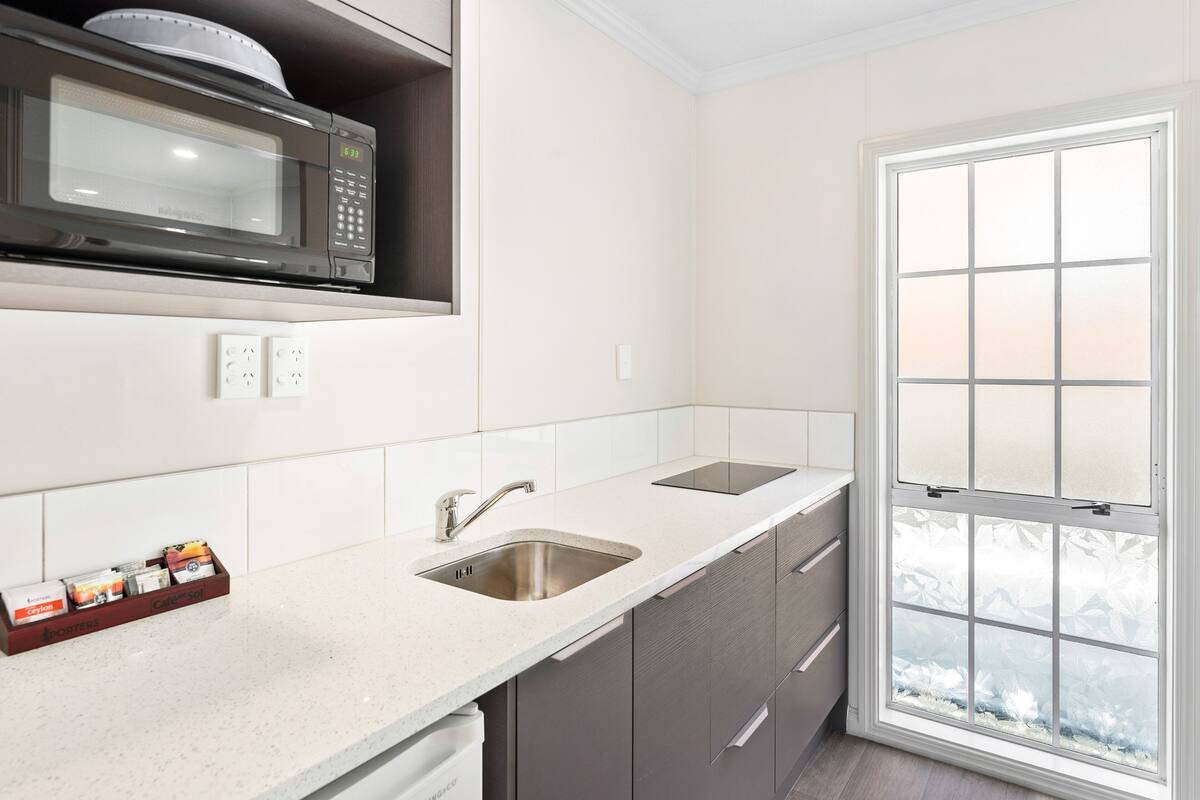 A kitchen with a microwave, two sinks, a window with frosted glass, and a cabinet with a spice rack.