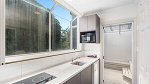 A modern kitchen with a built-in microwave, a sink, and a window overlooking a garden. - Ashleigh Court Motel (Rotorua)