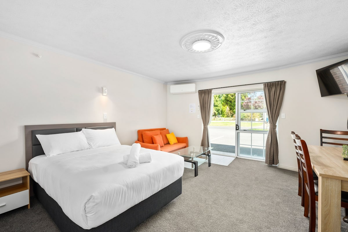 A hotel room with a bed, a sofa, a dining table, and a TV.