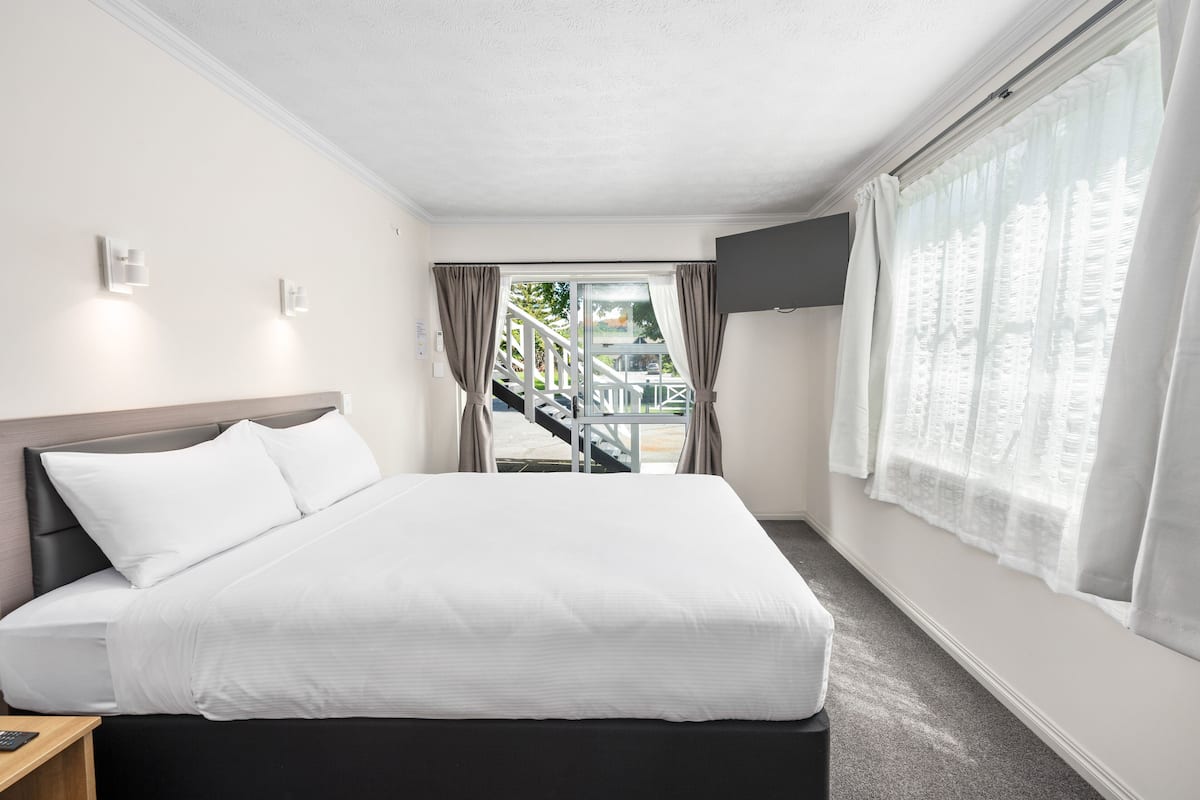 A hotel room with a bed, a TV mounted on the wall, and a view of the outside.
