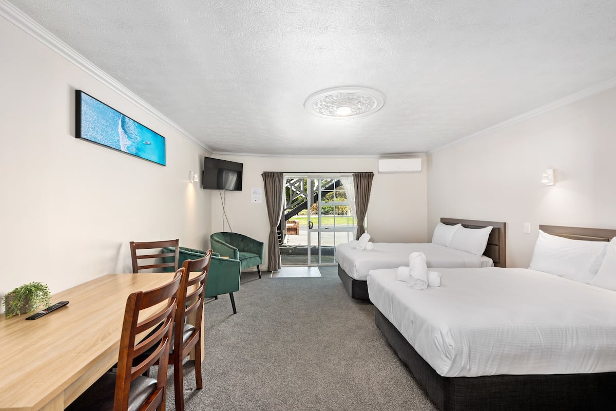 A hotel room with two beds, a desk, a TV, and a view of the outdoors.