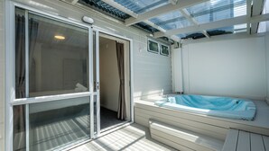 A sunlit room with a sliding glass door, a built-in hot tub, and a ceiling with skylights. - Ashleigh Court Motel (Rotorua)