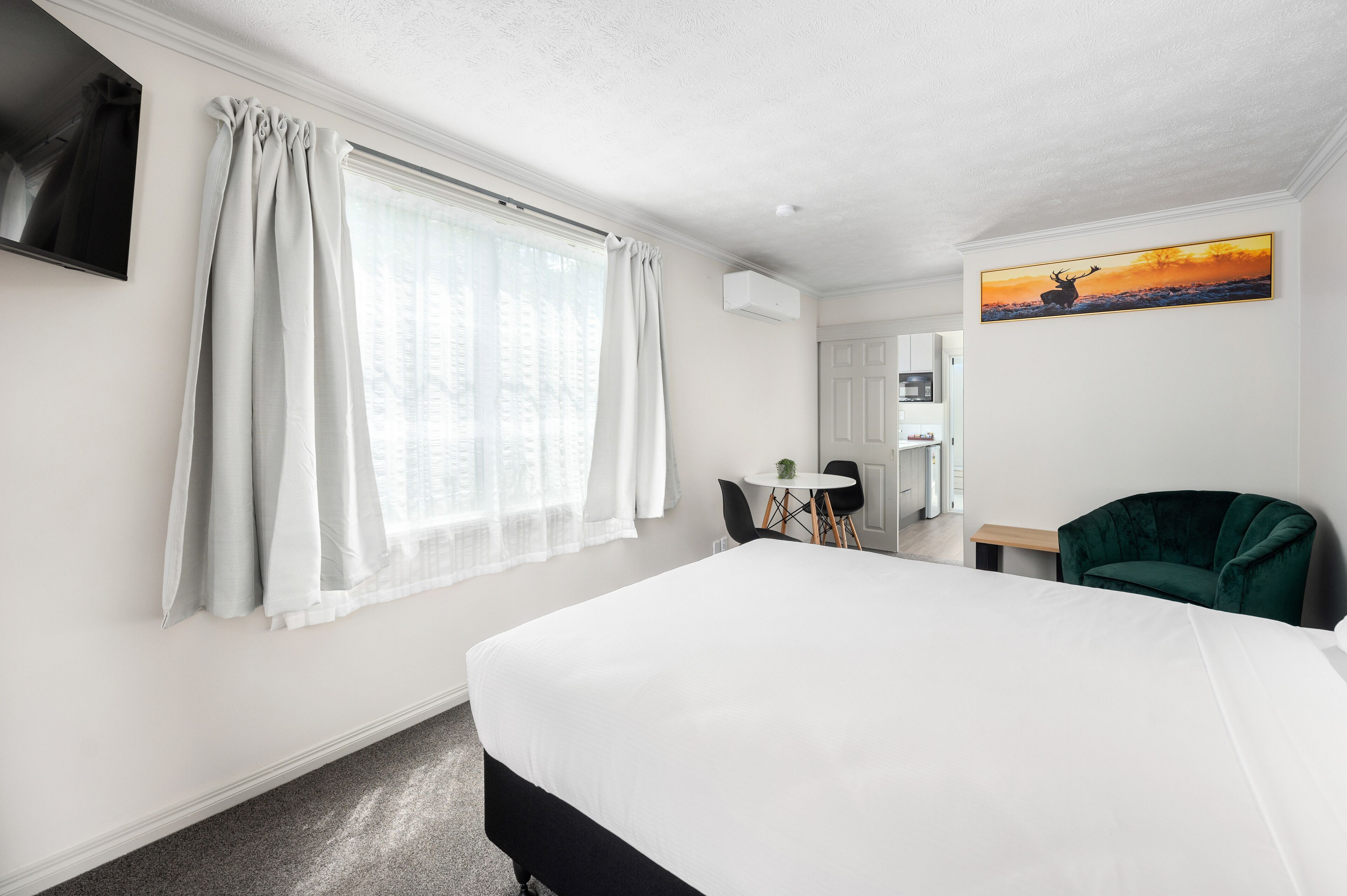 A hotel room with a large bed, a desk, a chair, and a painting on the wall.