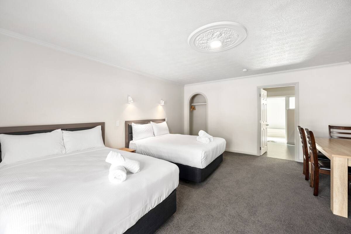 A hotel room with two beds, a dining table, and a mirror.
