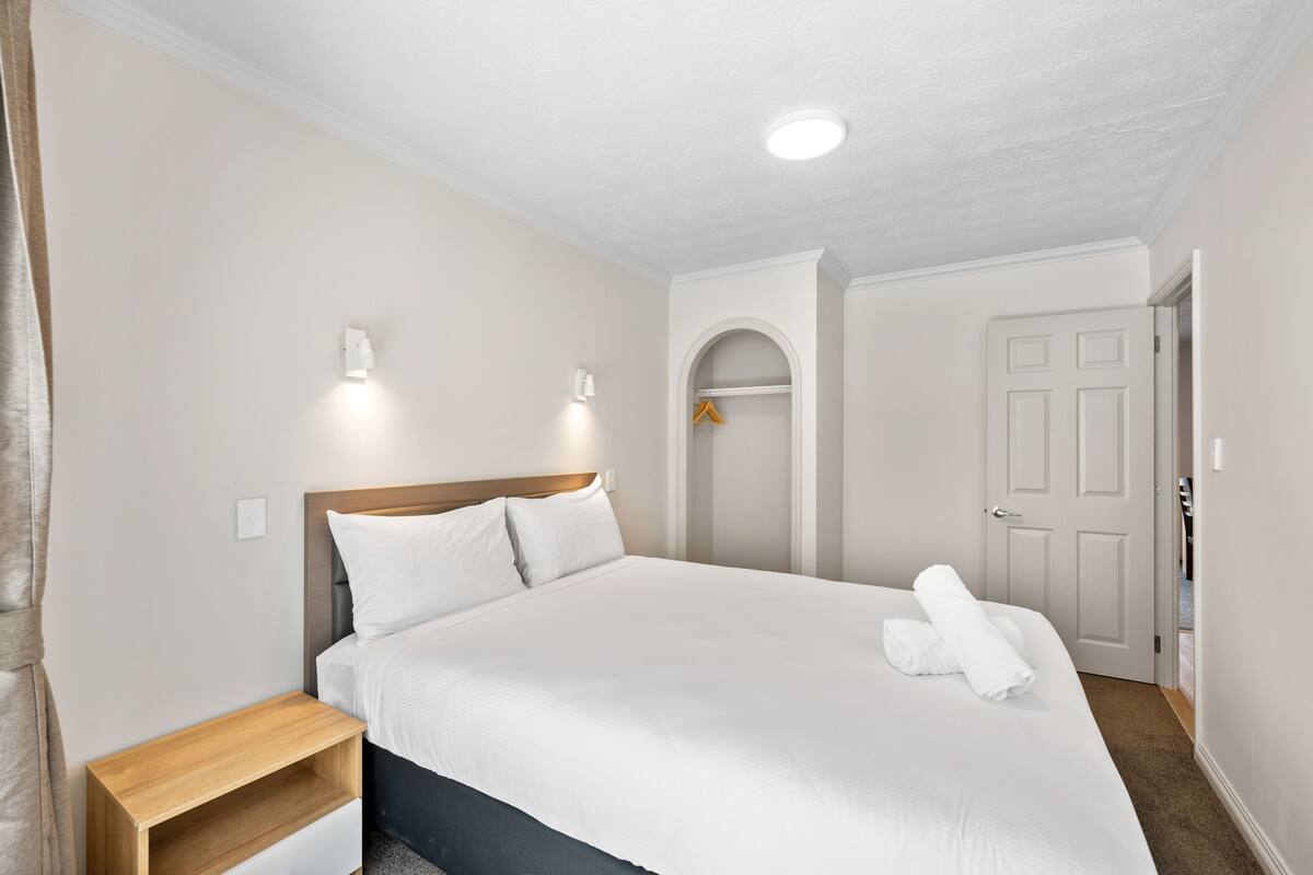 A hotel room with a bed, bedside table, wardrobe, and a door leading to another room.
