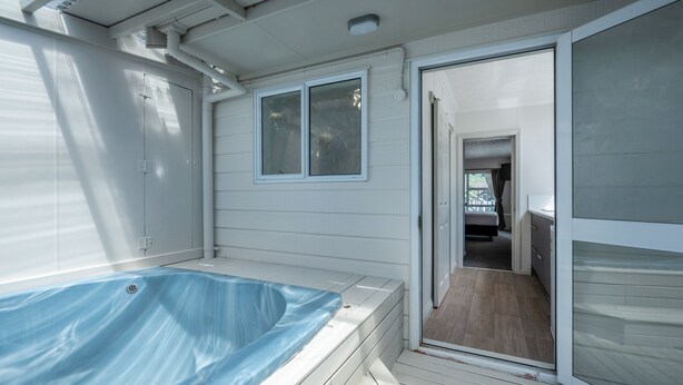 A covered outdoor swimming pool with a hot tub, wooden deck, and a sliding glass door leading to a room with a wooden floor and a bed. - Ashleigh Court Motel (Rotorua)