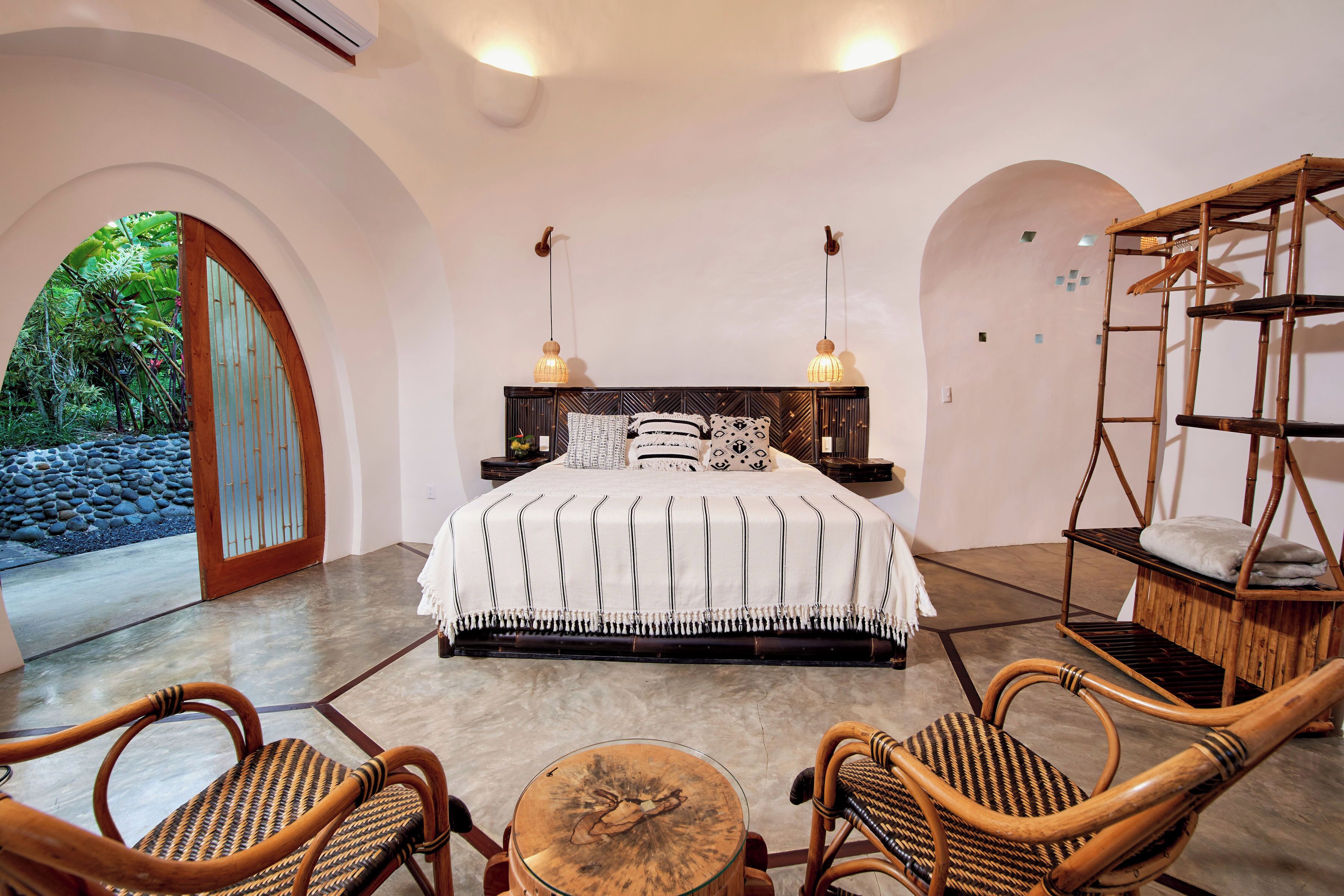 A bedroom with a bed, two chairs, a small table, and a hanging chair.