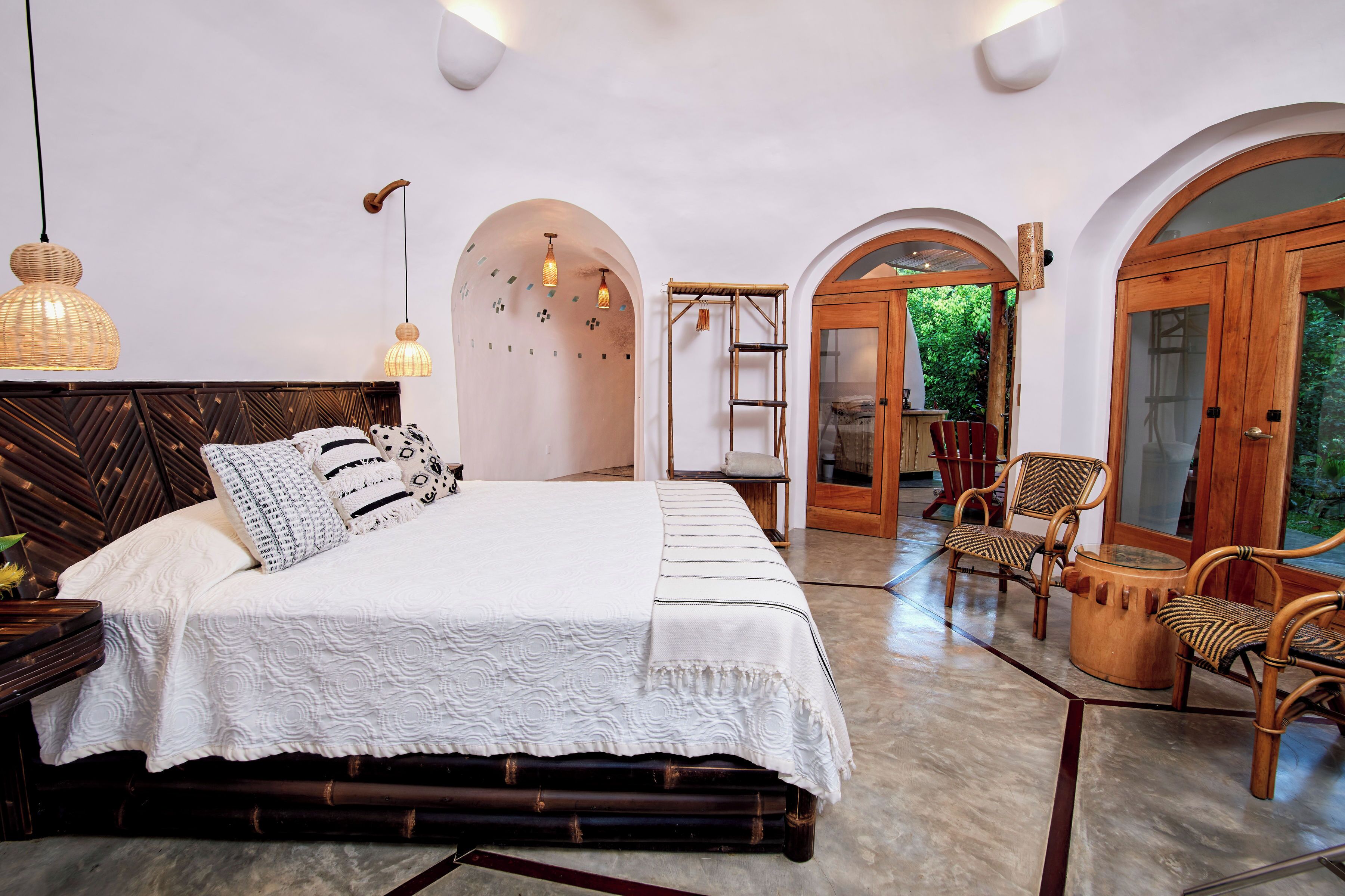 Un dormitorio amplio con una cama grande, cabecera de madera y vistas al jardín a través de un arco.
