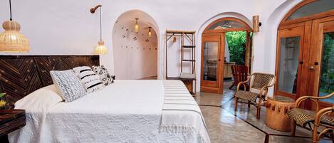 Un dormitorio amplio con una cama grande, cabecera de madera y vistas al jardín a través de un arco.