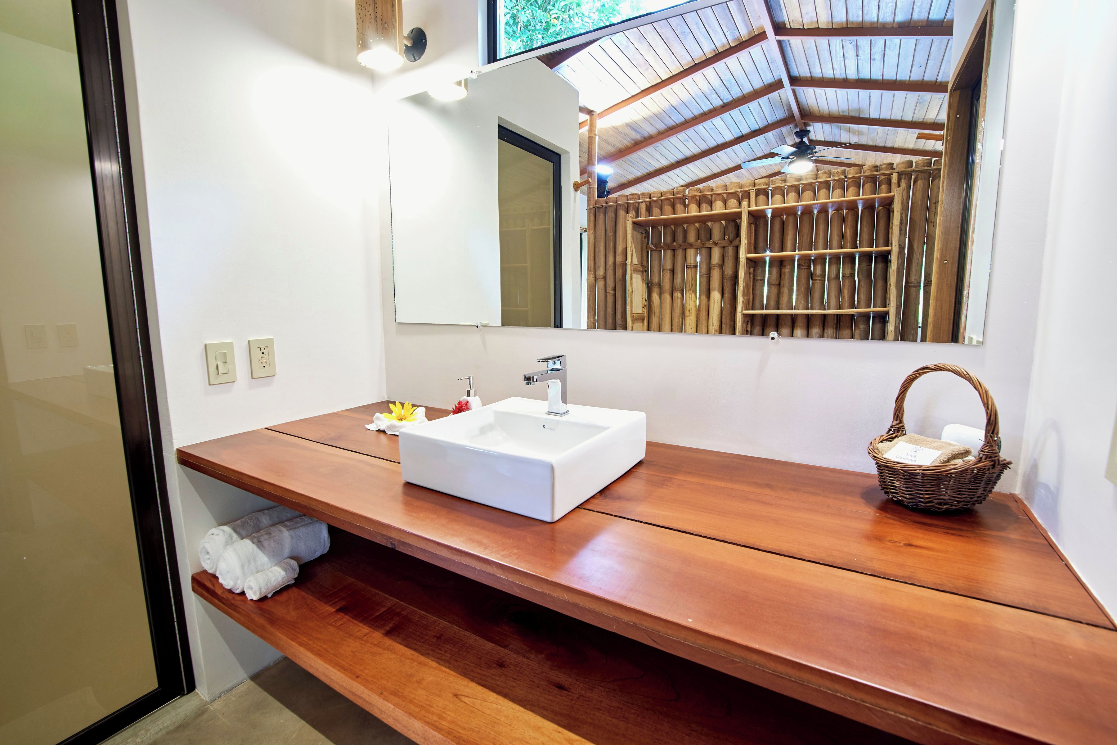 A bathroom with a wooden vanity, a white sink, a mirror, and a ceiling fan.