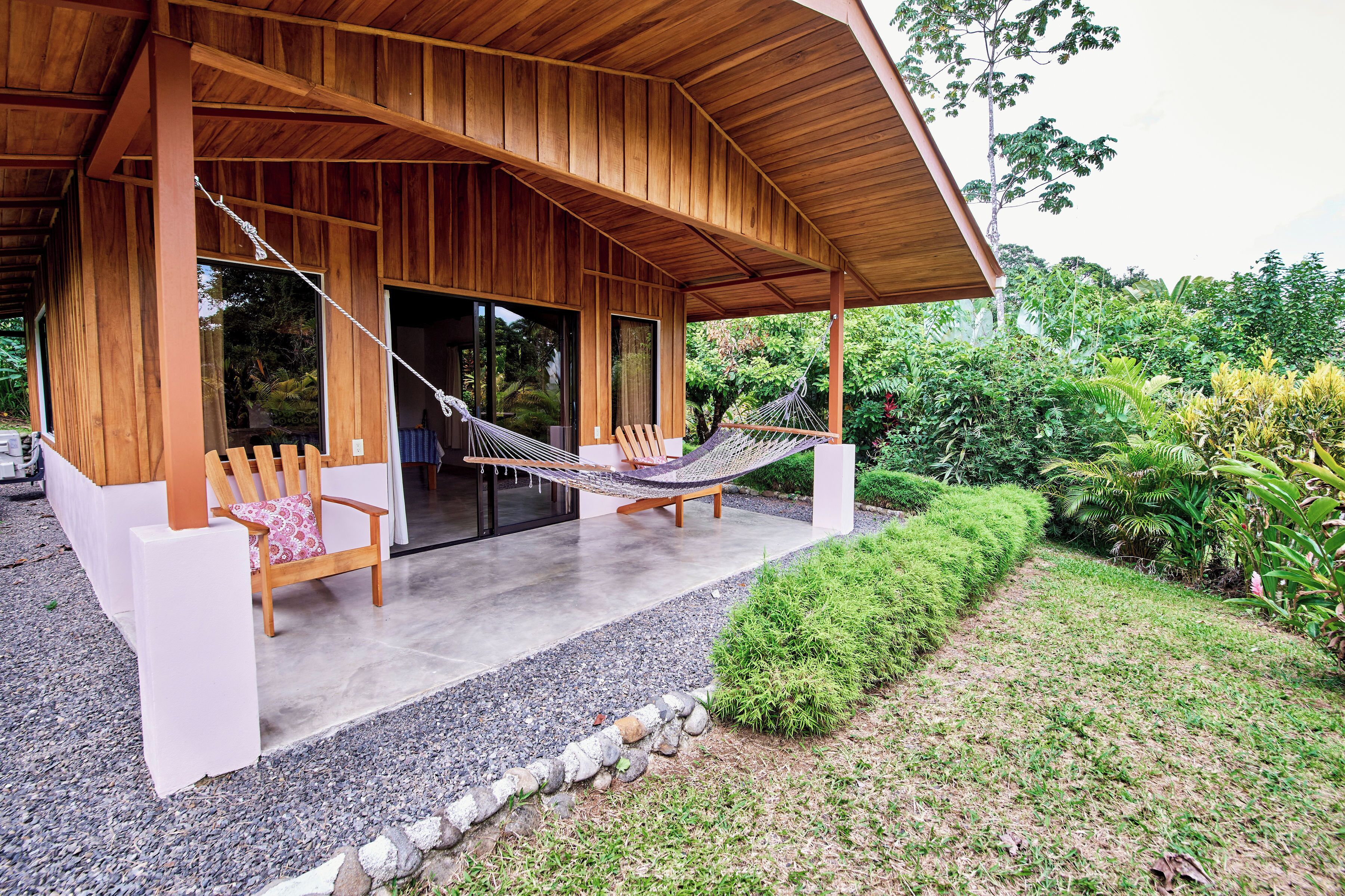 A wooden covered patio with two wooden chairs and a hammock.