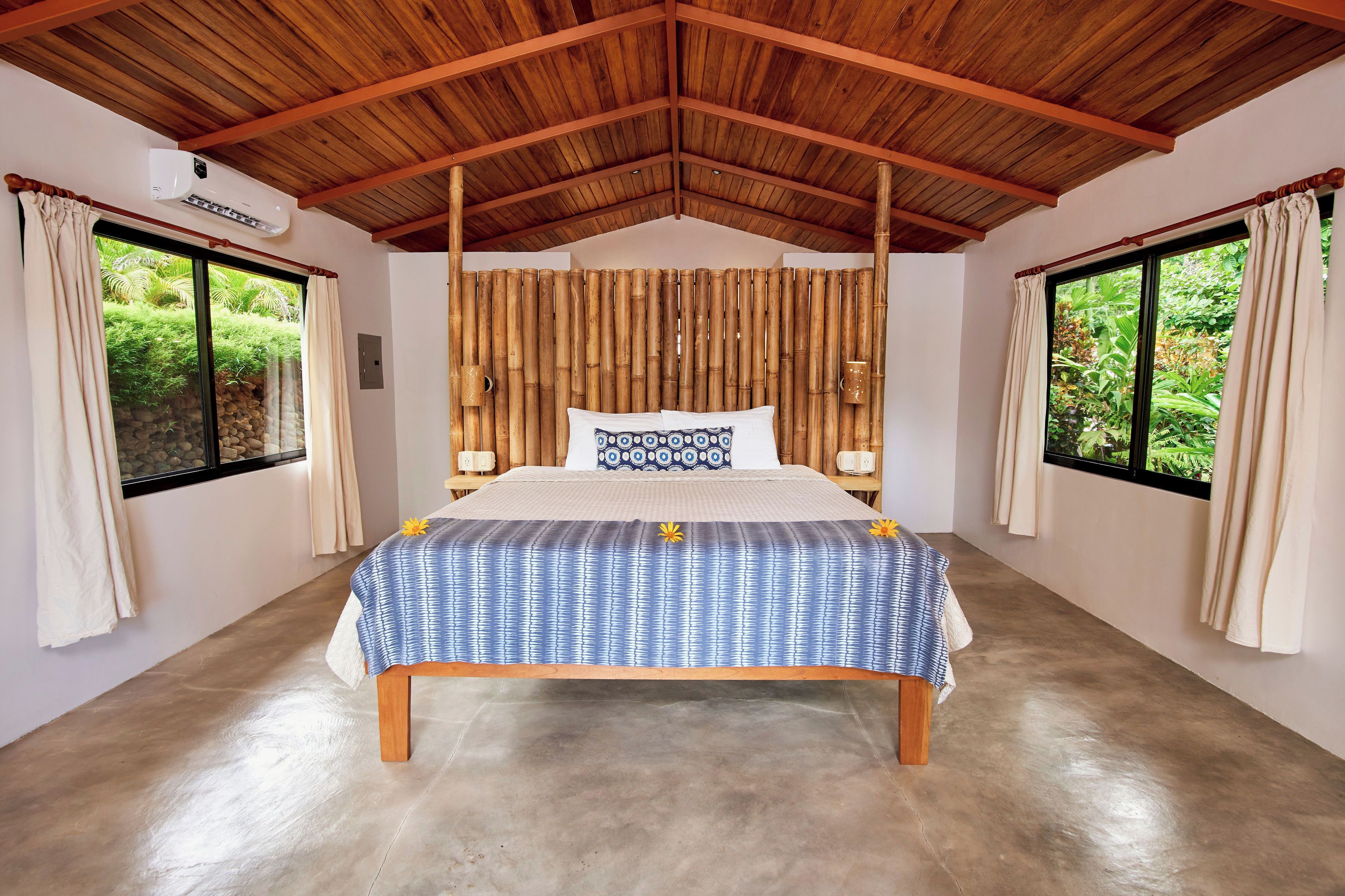 Un dormitorio con cama, techo de madera y ventanas grandes.