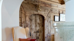 A cozy room with a wooden chair, a red patterned sofa, and a stone pillar. - Hotel Angela (Lech am Arlberg)