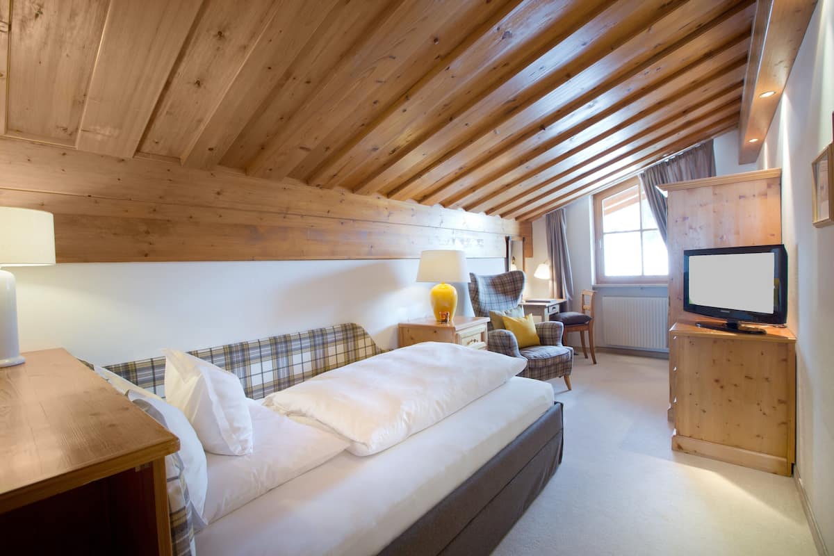 A cozy room with a bed, a desk, a chair, a television, and a window.