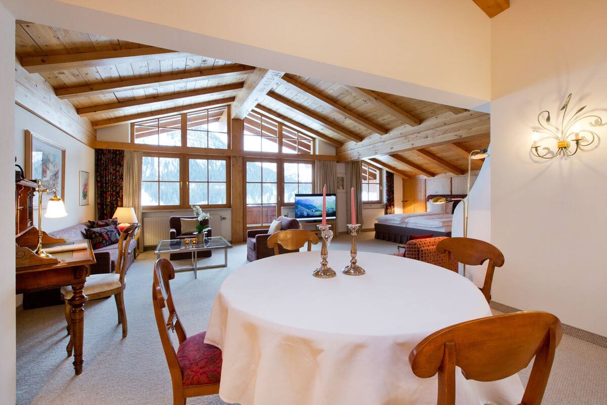 A cozy room with a wooden ceiling, a round table with chairs, a TV, and a bed.