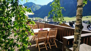 An outdoor dining area with wooden tables and chairs, overlooking a mountainous landscape. - Hotel Angela (Lech am Arlberg)