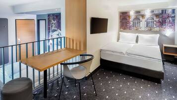 A hotel room with a bed, a desk, a chair, a TV, and a window with a view of buildings.