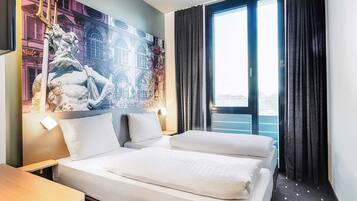 Habitación de hotel con una cama grande, un escritorio y vistas a edificios a través de una ventana.