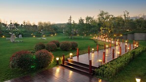 Un espacio exterior bien iluminado con una terraza de madera, estructuras de piedra y vegetación.