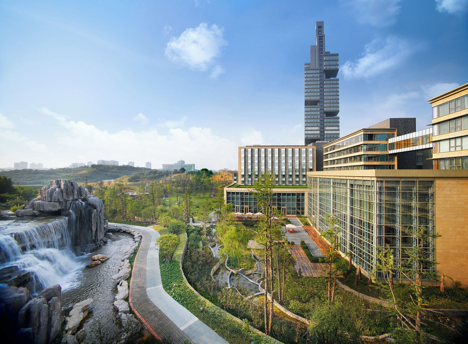 A modern building complex with a waterfall feature, surrounded by greenery and a clear sky.
