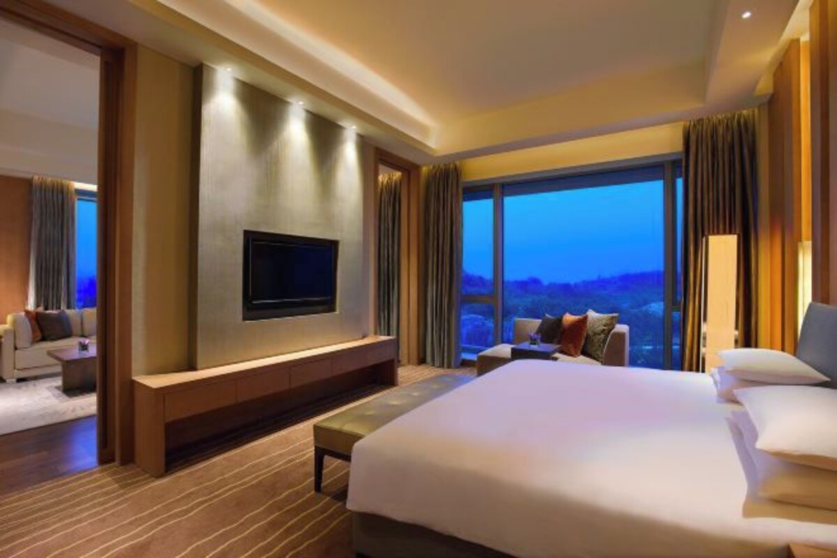 Habitación de hotel moderna con una cama grande, un televisor de pantalla plana montado en la pared y un ventanal con vistas panorámicas.