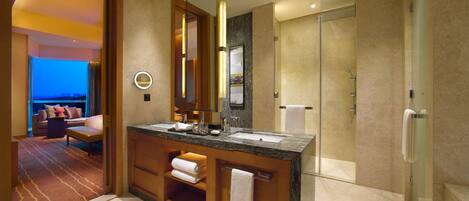 Un baño moderno con un espejo grande, un lavabo y una ducha. Se observa un perchero con toallas y una puerta de vidrio para la ducha.