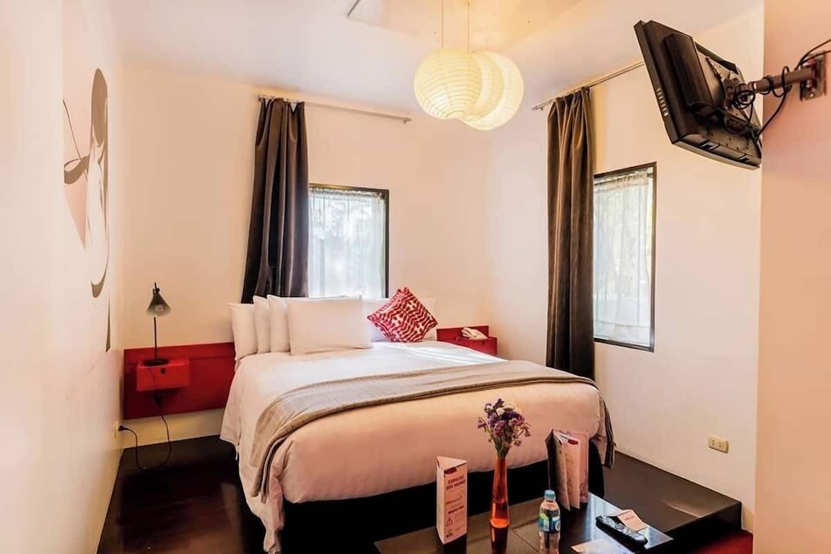 Ett hotellrum med en säng, ett sängbord, en lampa och en tv som är monterad på väggen.