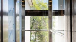 An elevator with glass doors, a wooden floor, and a view of trees outside. - Dreams Boutique Hotel (Arequipa)