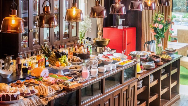 A buffet with a variety of food items and beverages, including fruits, pastries, and a red refrigerator in the background. - Dreams Boutique Hotel (Arequipa)