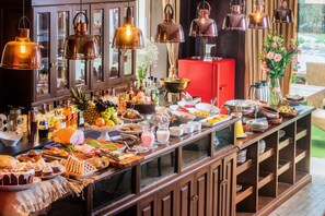 Een buffet met diverse soorten eten en drinken, waaronder fruit, gebak en een rode koelkast op de achtergrond.