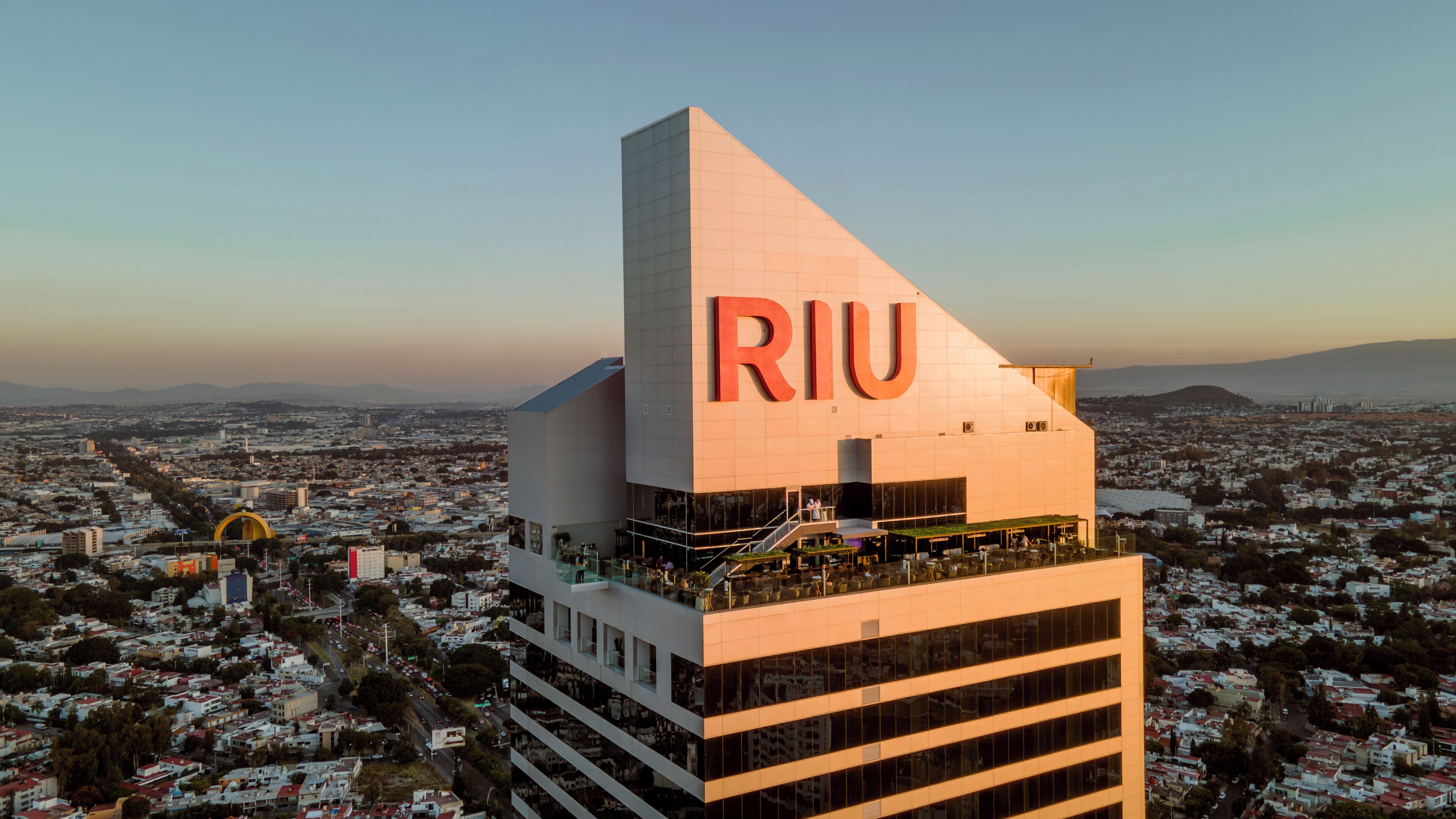 Un edificio moderno con un llamativo letrero de 'RIU', rodeado por un paisaje urbano.