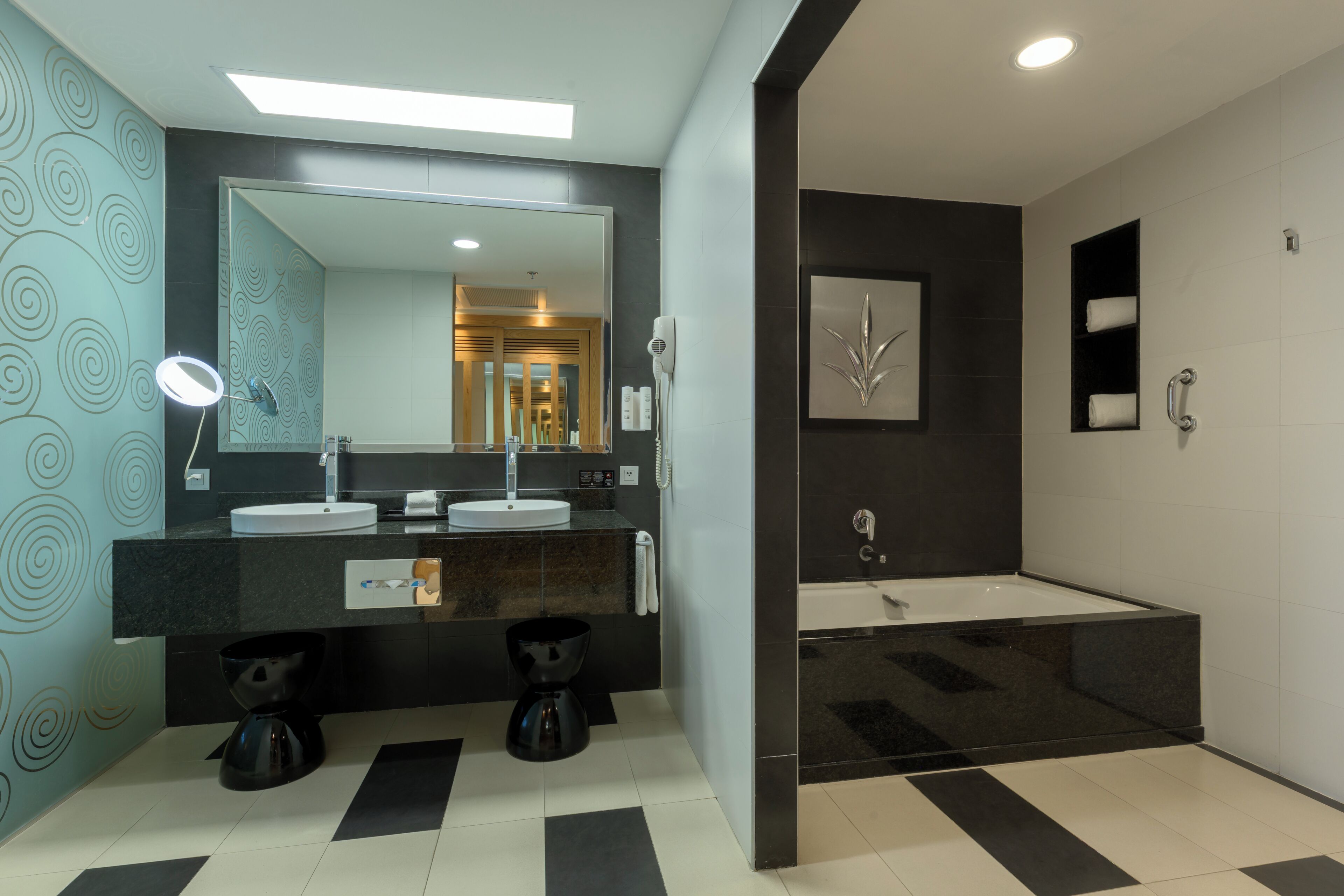A modern bathroom with a large mirror, two sinks, a bathtub, and a coffee machine.