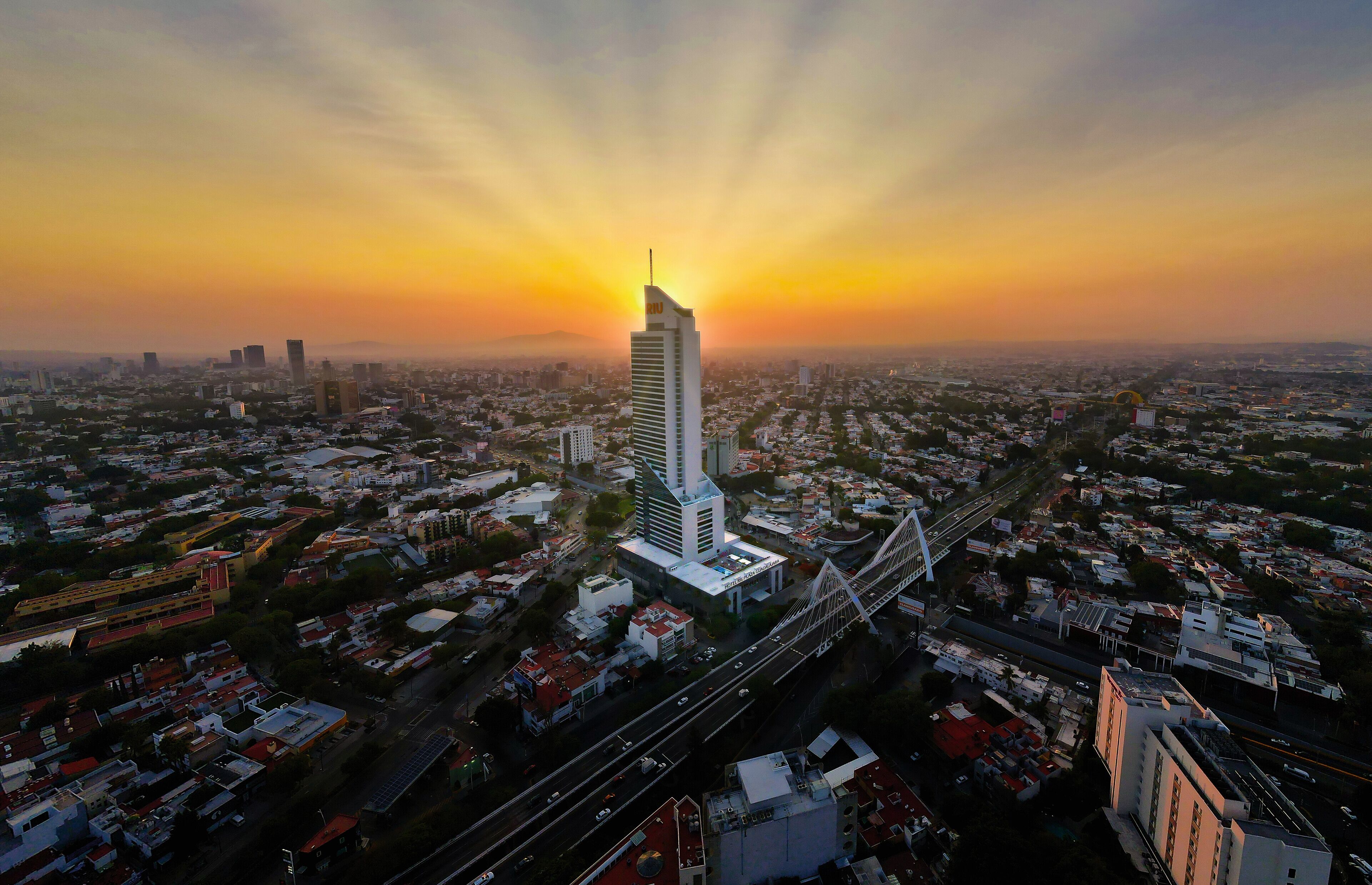 An aerial view of a cityscape with a prominent skyscraper, roads, and surrounding buildings.