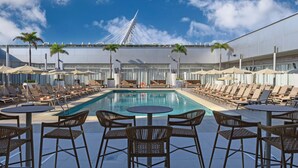 A poolside area with lounge chairs, tables, and umbrellas, overlooking a modern bridge.