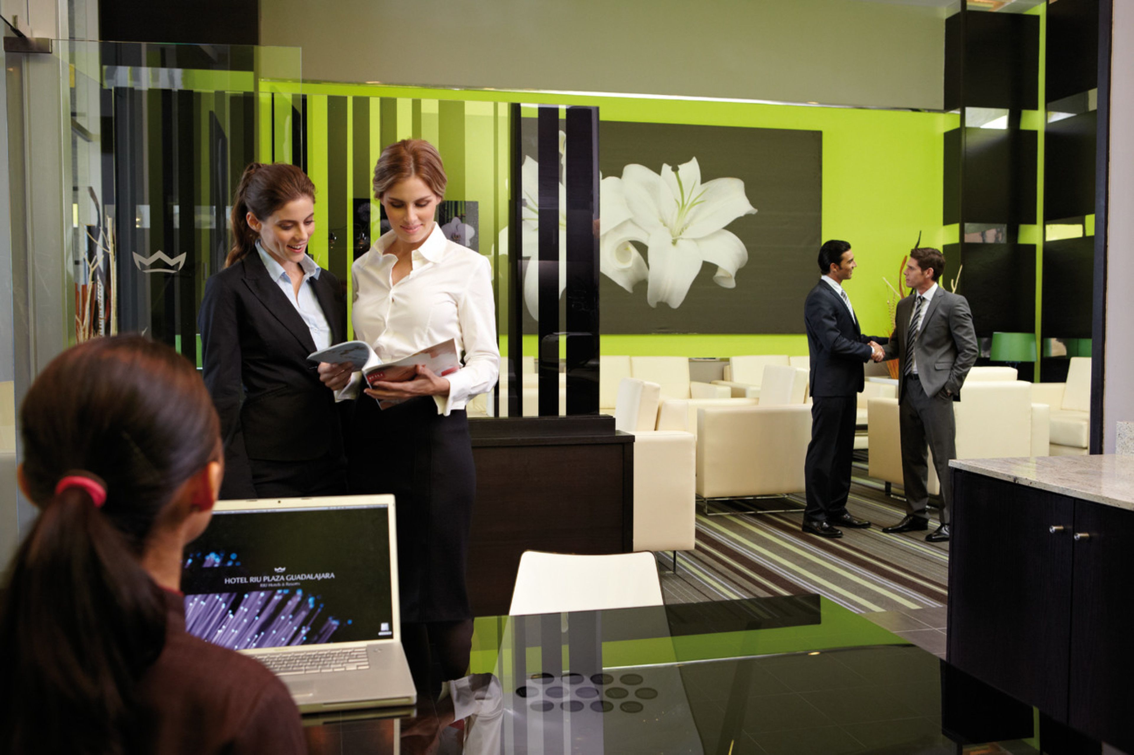 Una hall d'hotel moderna con schema colori verde e nero, un'ampia opera d'arte floreale e un'area salotto con divani bianchi.