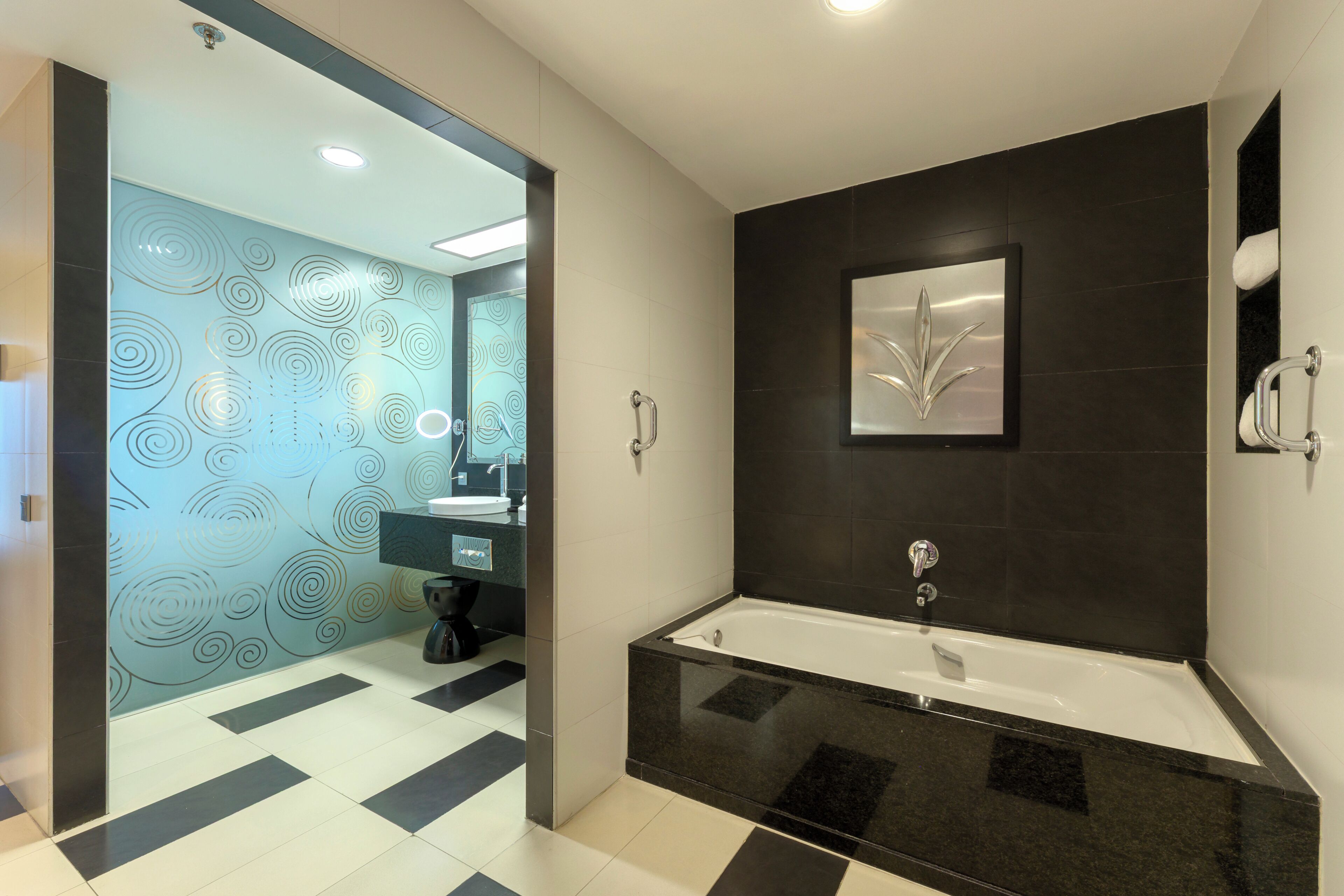Un baño moderno con una bañera negra, un espejo grande y un papel tapiz estampado.