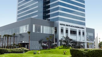 Un hotel moderno con una amplia fachada de vidrio, una entrada destacada y una escultura de caballos al frente.
