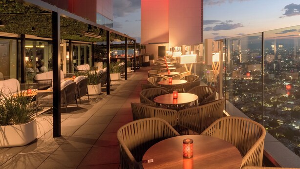 An outdoor seating area with wicker chairs and tables, overlooking a cityscape.