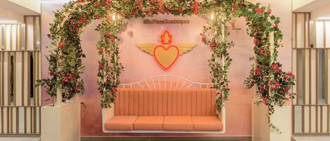Una habitación con un letrero de neón en forma de corazón, un banco y una pared cubierta de plantas trepadoras.