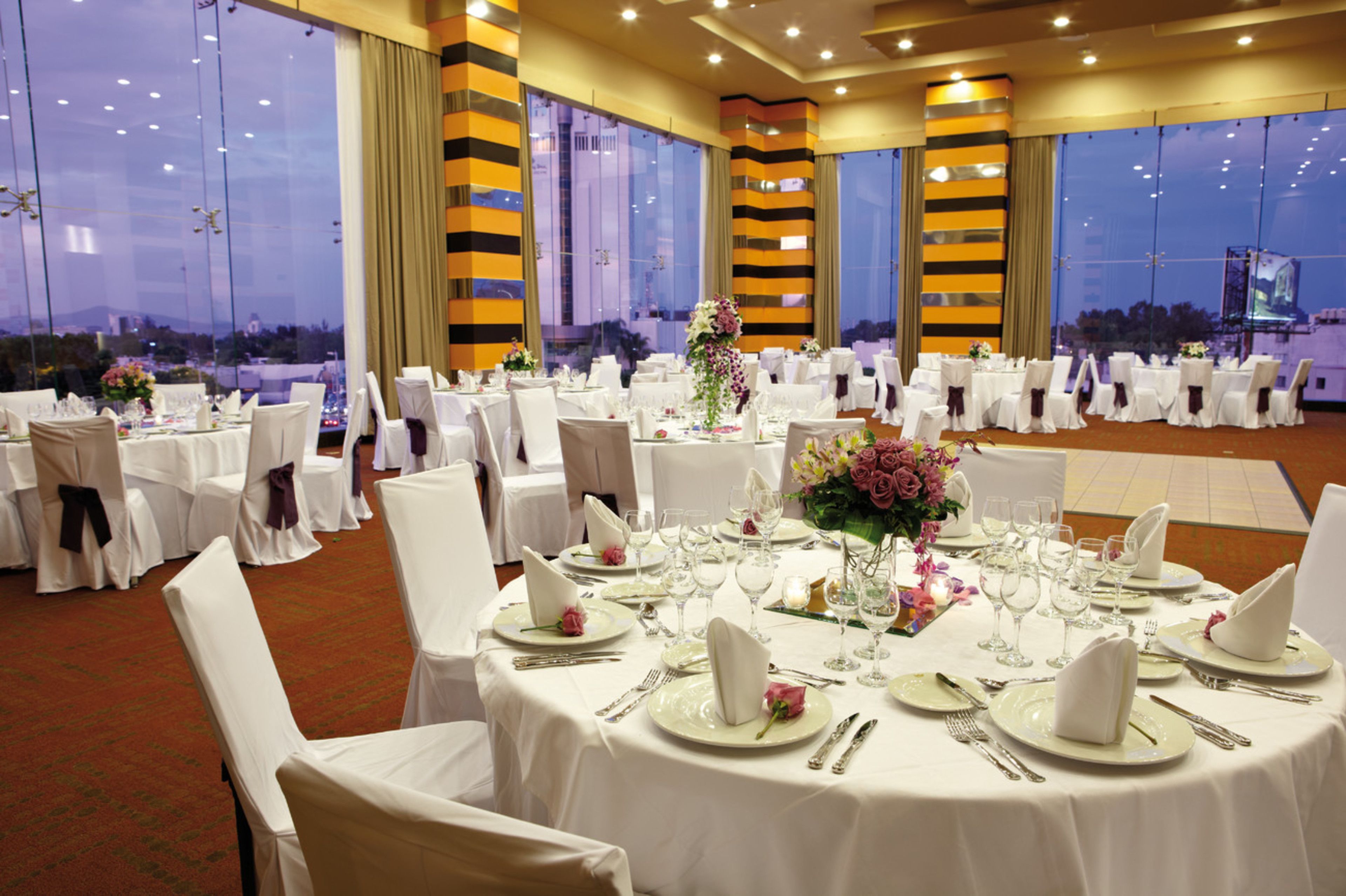 A banquet hall with round tables set for a formal event, featuring white tablecloths, chairs, and floral centerpieces.