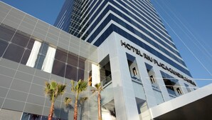 A modern hotel building with a glass facade and palm trees in front.