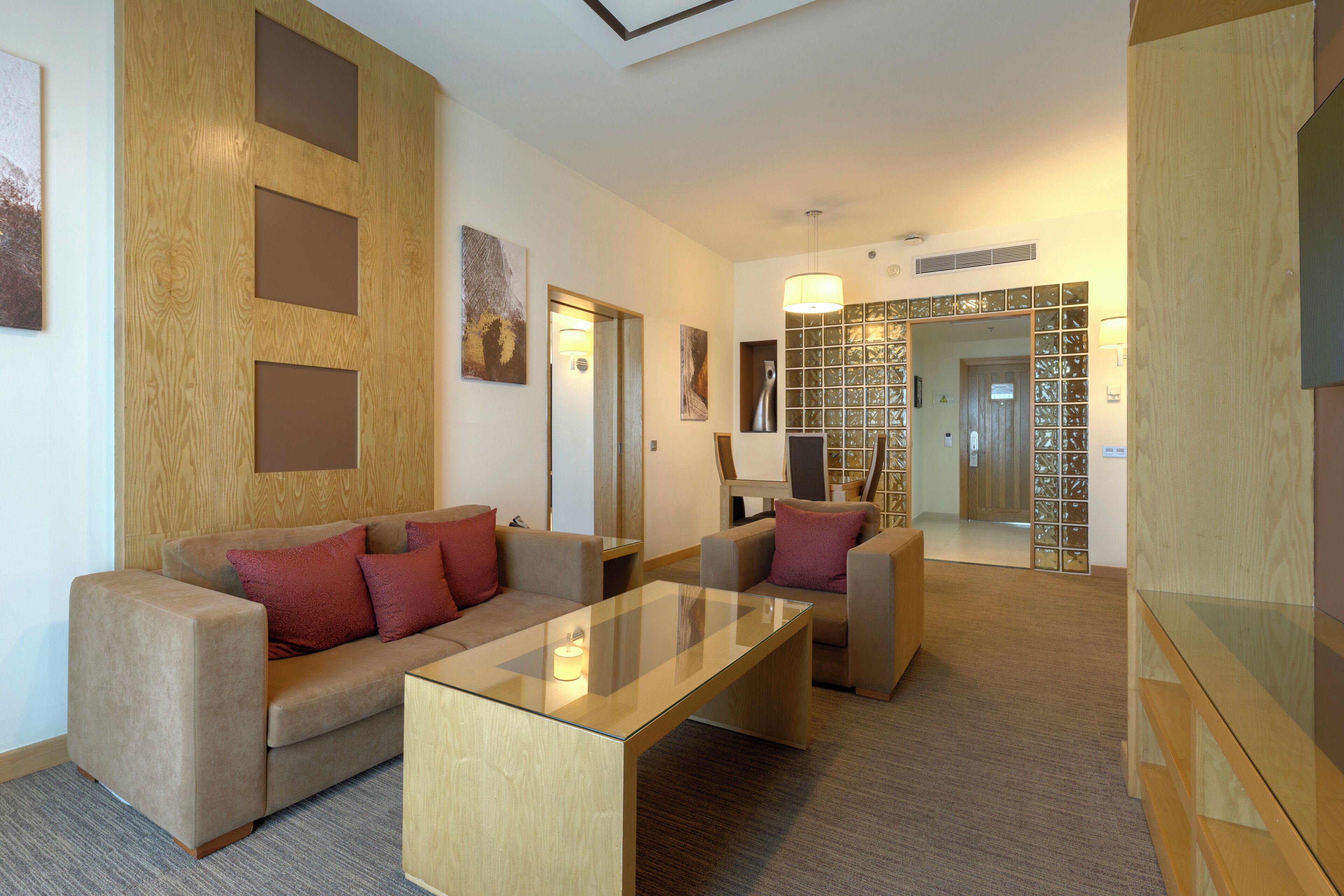 Una sala de estar moderna con una mesa de centro de vidrio, dos sofás con cojines rojos y una pared de acento de madera.