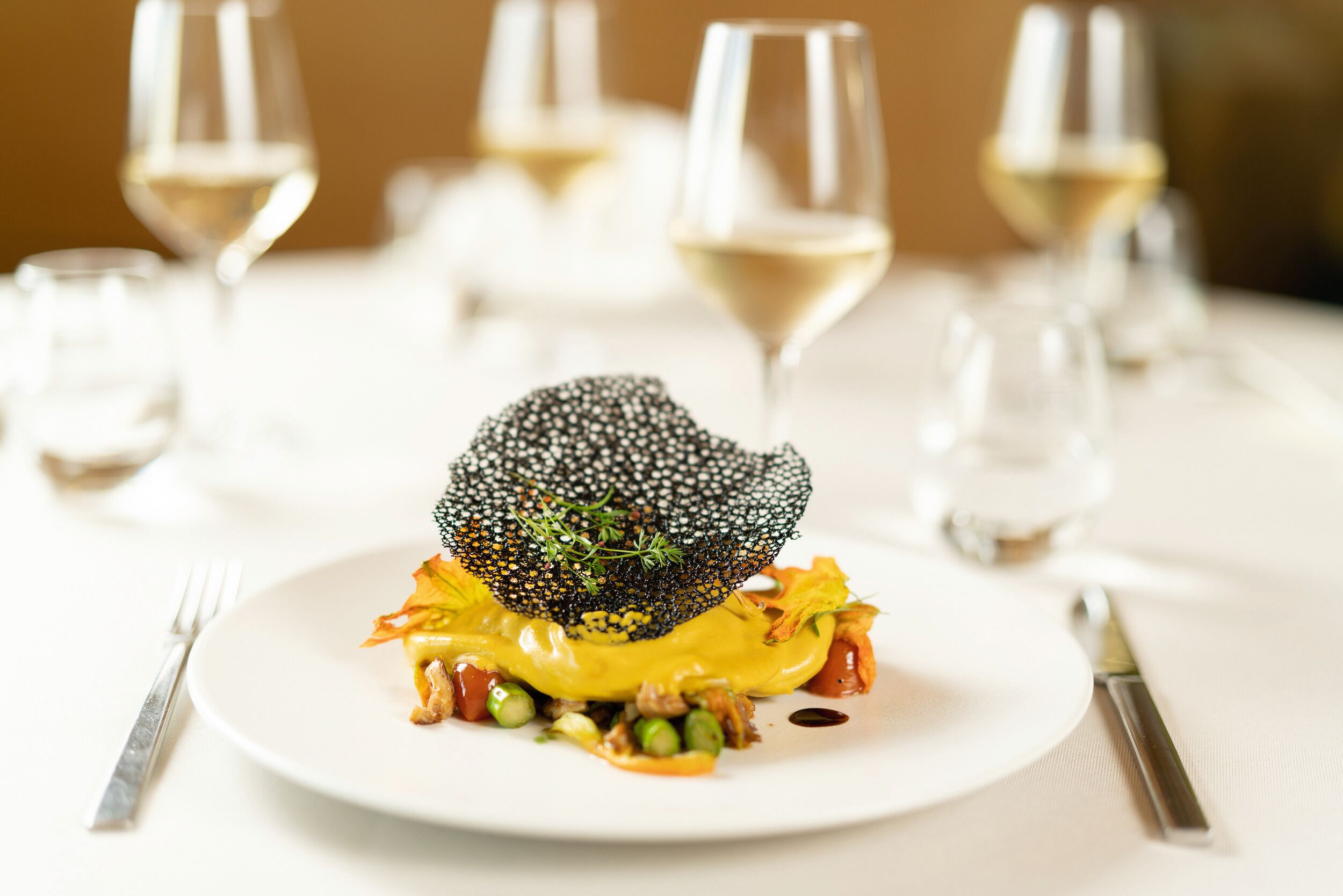 Un plato con una presentación gastronómica original, rodeado de copas de vino sobre una mesa.