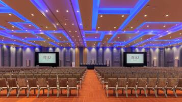 A conference room with rows of chairs, two large screens, and a wooden floor.