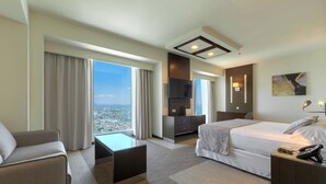 A hotel room with a bed, a desk, a chair, a TV, and a view of the city.