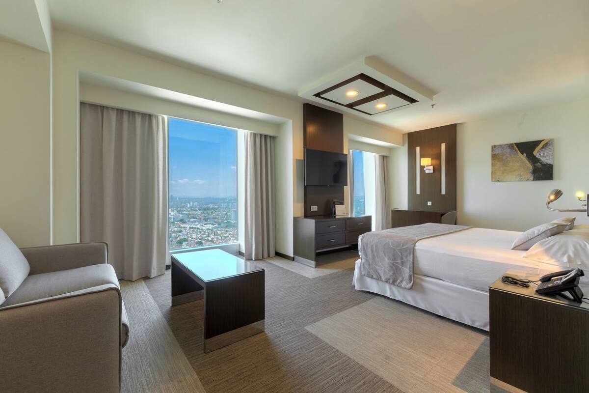Une chambre d’hôtel avec un lit, un bureau, une chaise, une télévision et une vue sur la ville.