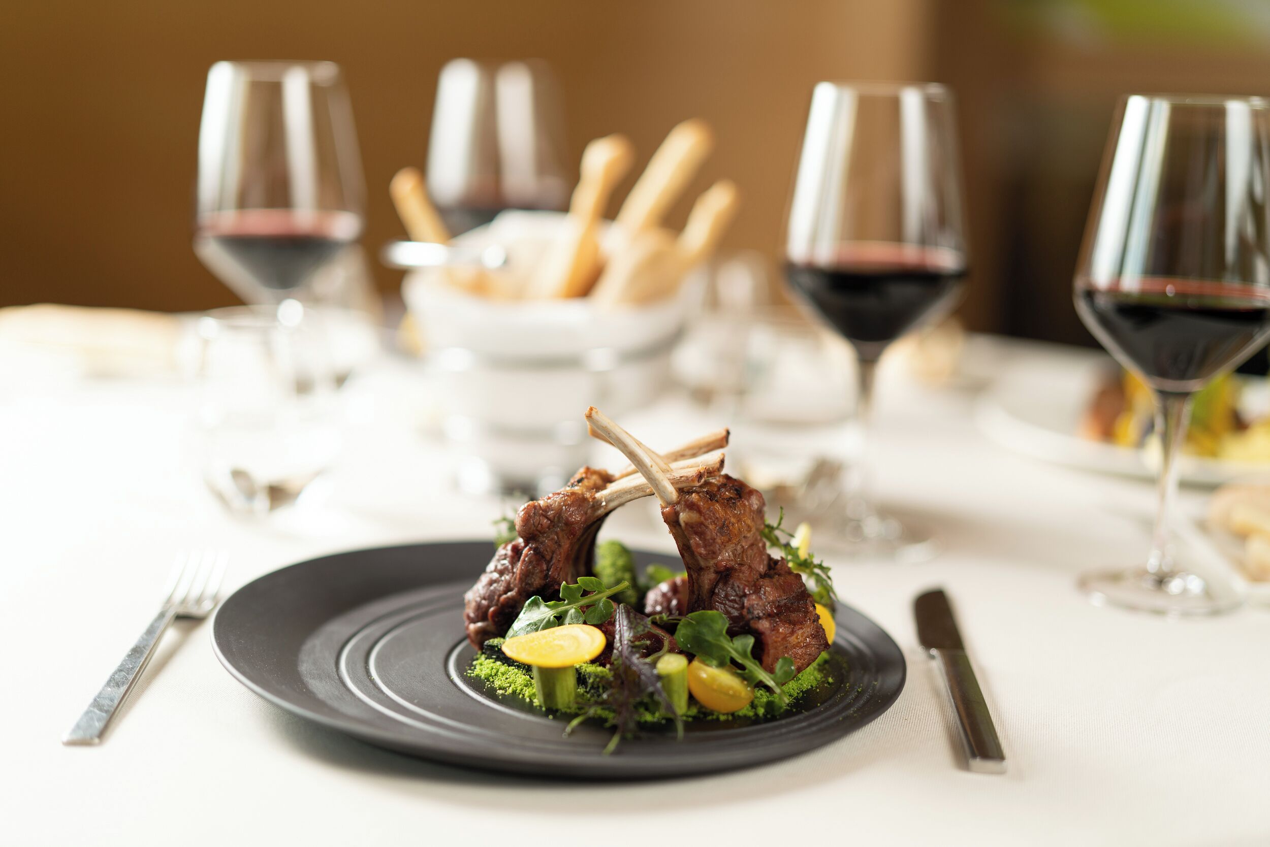 Una mesa de comedor con un plato de comida, copas de vino y cubiertos.