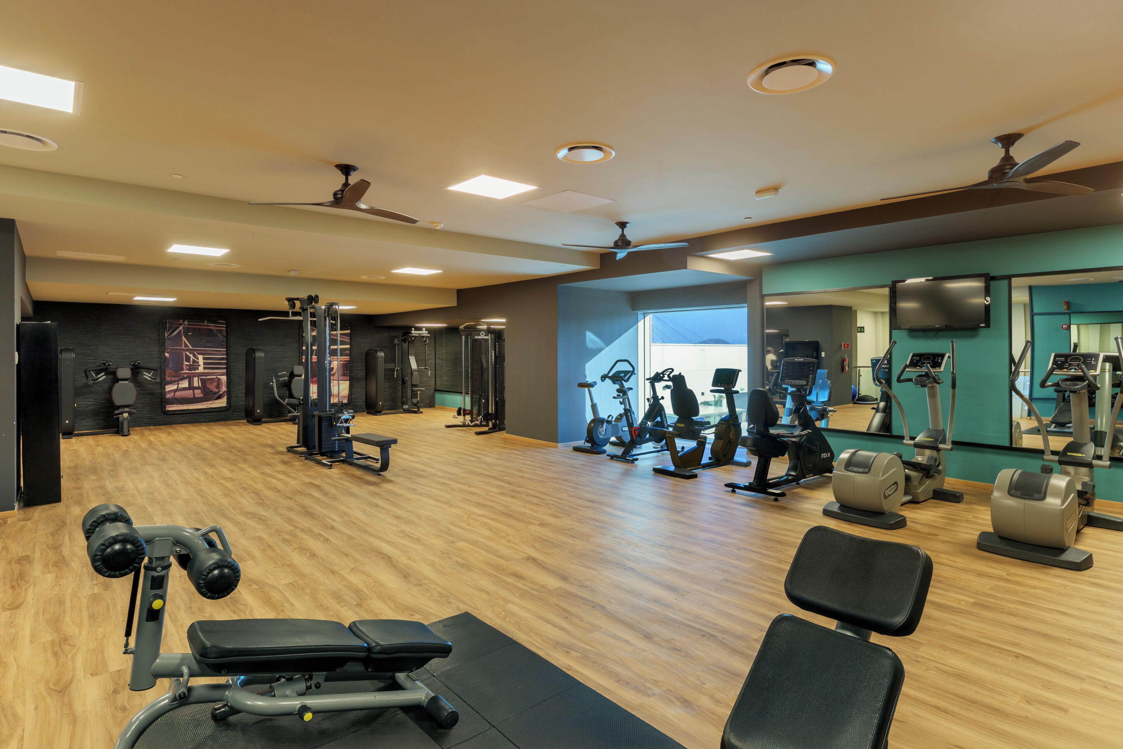 Un gimnasio con diverso equipo de ejercicio, suelo de madera y ventiladores de techo.